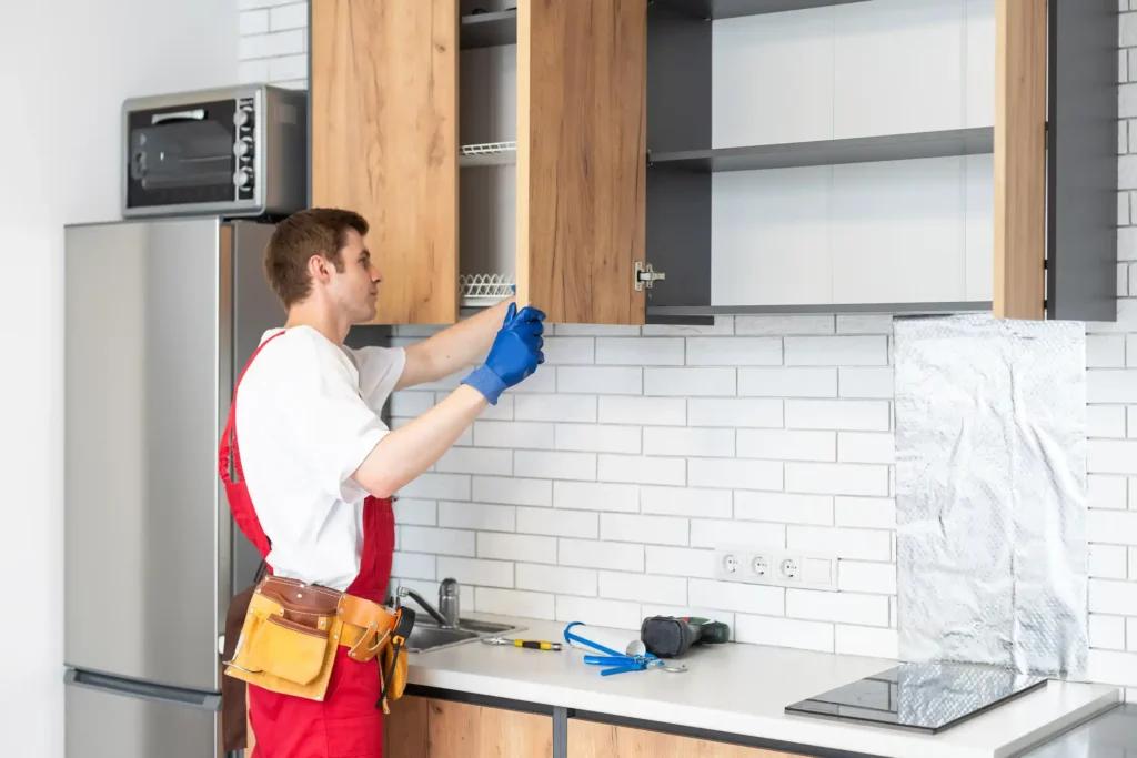 Experienced handyman fixing broken kitchen cabinet door and replacing damaged hinges with new hardware in modern Dubai kitchen ensuring proper alignment